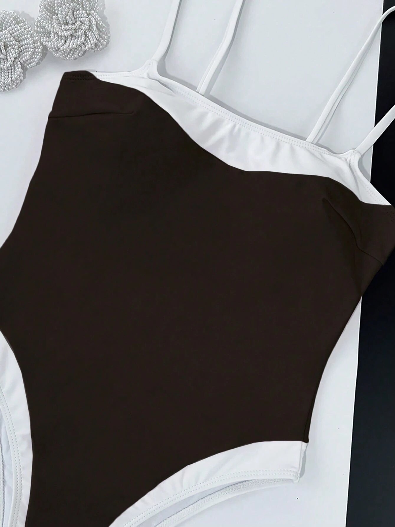 A dark brown one-piece swimsuit featuring white contrast trim along the scoop neckline and high-cut legs.