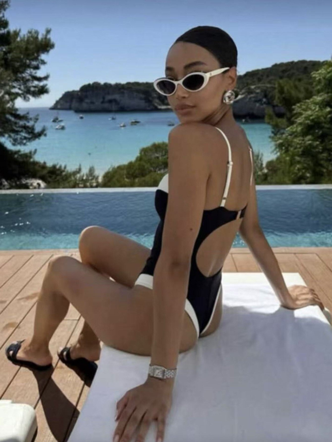 Model wearing a black and white contrast trim high-cut one-piece swimsuit with an open back.