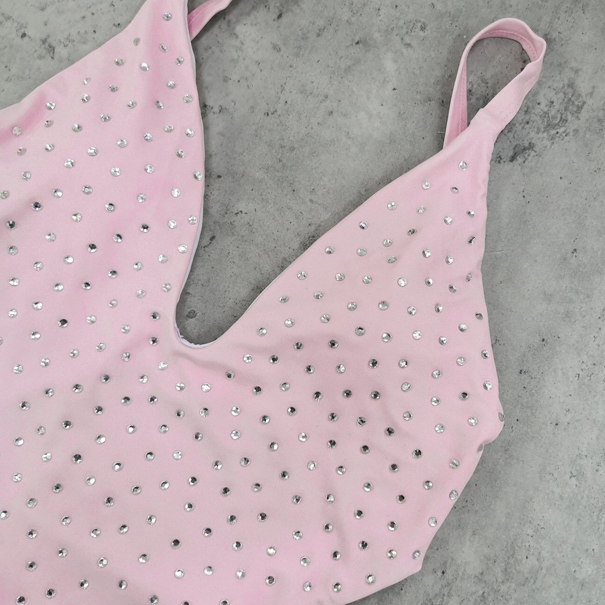 Close-up of a pink rhinestone-embellished one-piece swimsuit featuring a deep V-neckline and thin straps.