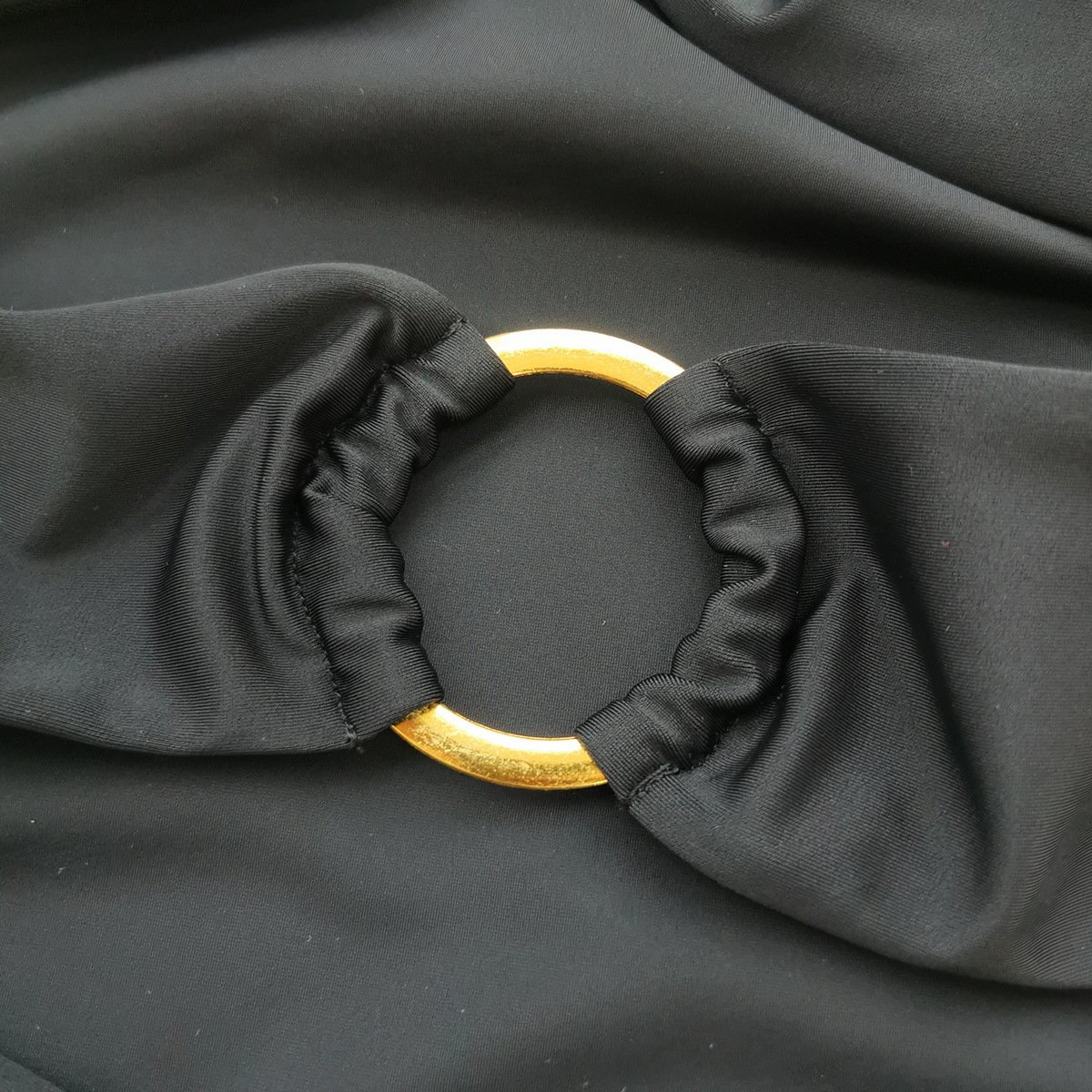 Close-up of a black strapless swimsuit featuring a gold ring hardware cutout with gathered fabric detailing.