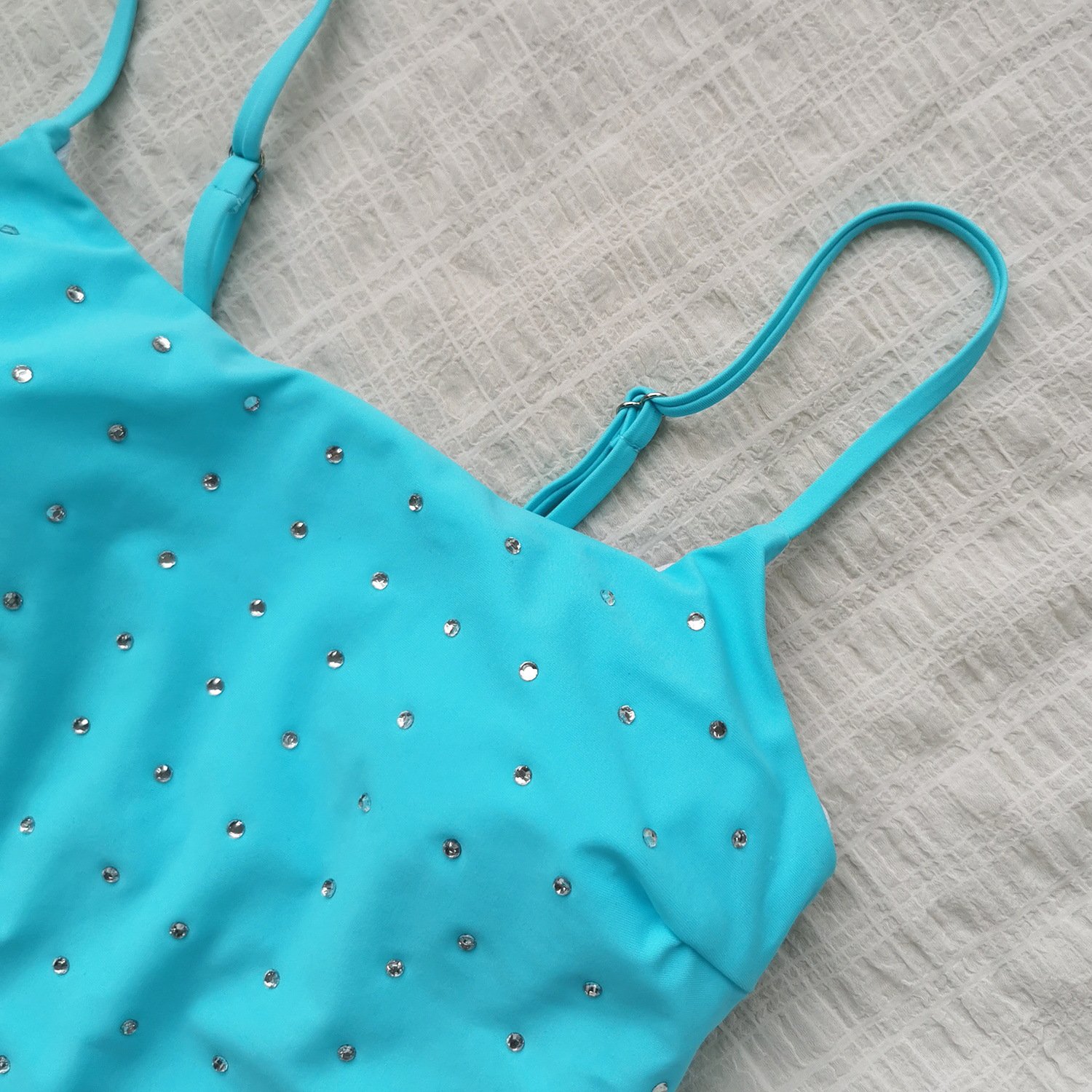 Turquoise one-piece swimsuit featuring rhinestone embellishments and adjustable spaghetti straps.
