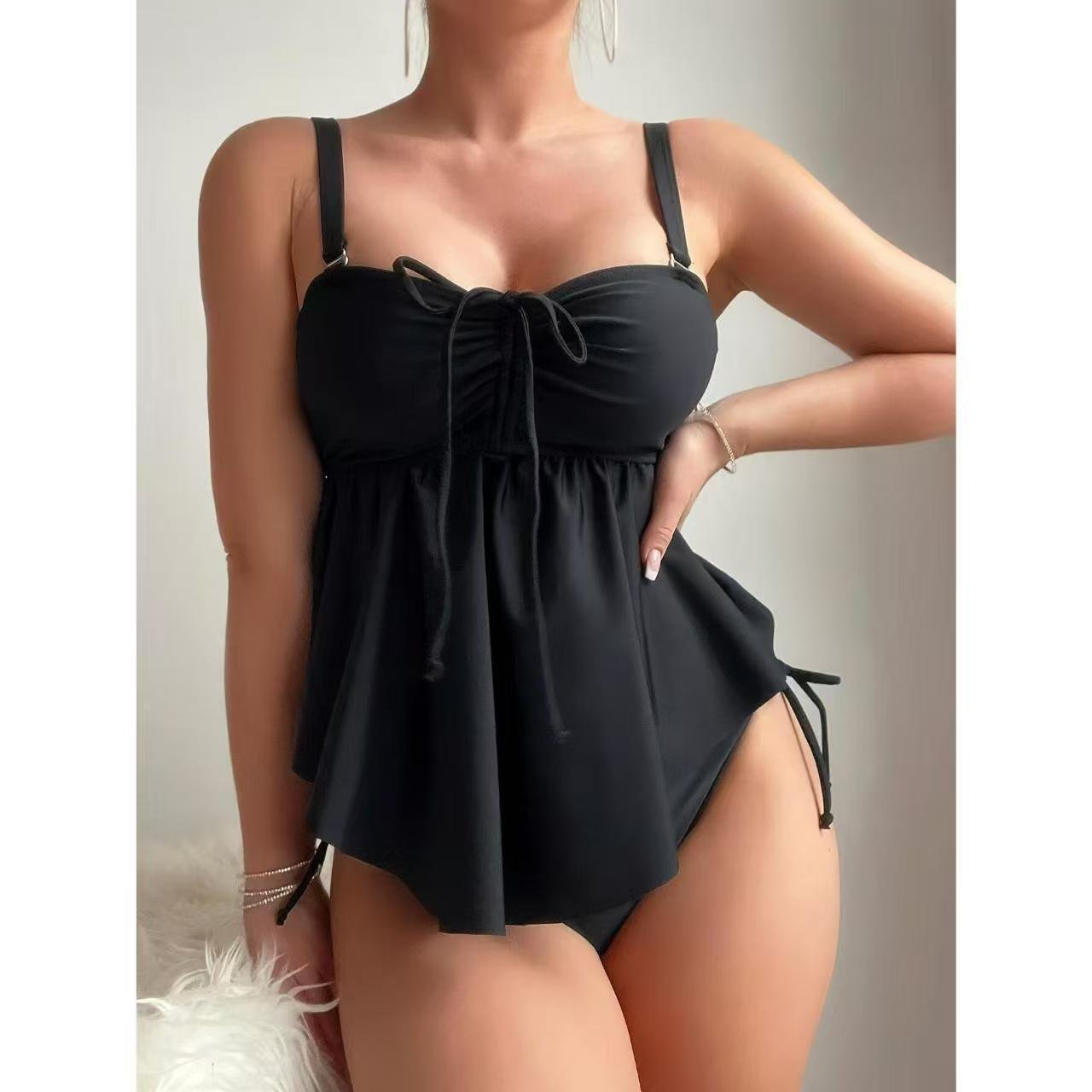 Black one-piece swimsuit with a sweetheart neckline, center front tie, and flared peplum skirt.