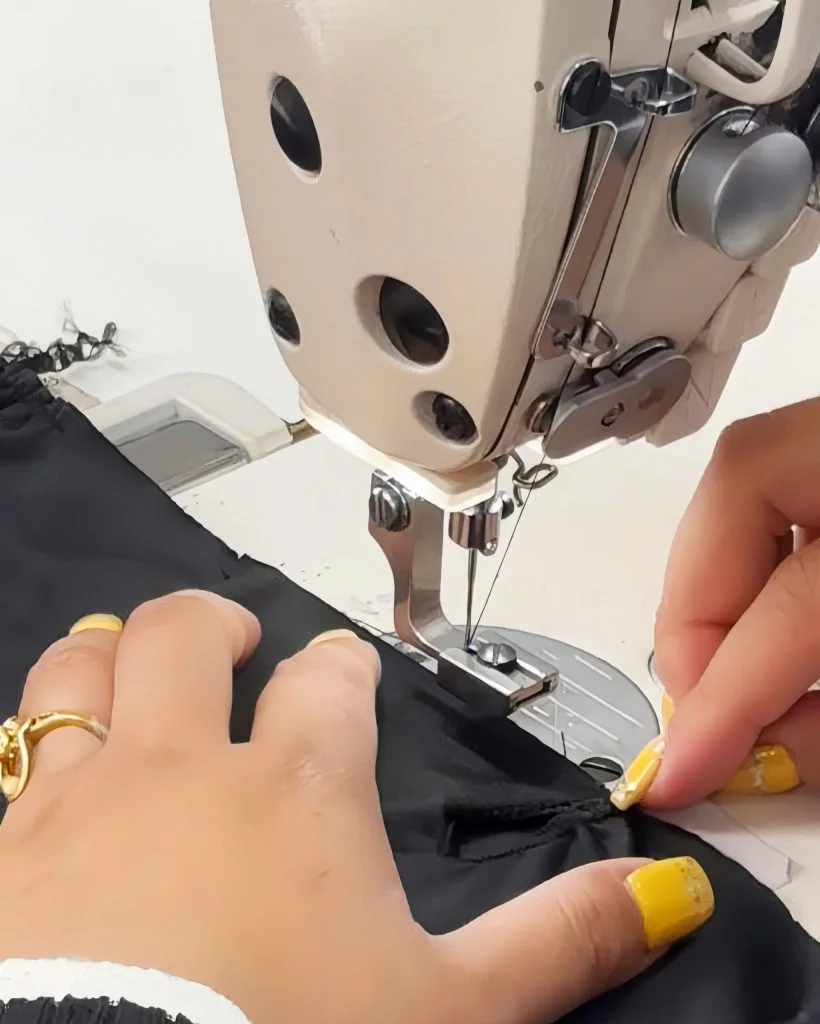 Close-up of hands guiding black swimwear fabric through industrial sewing machine during production at swimwear manufacturer.