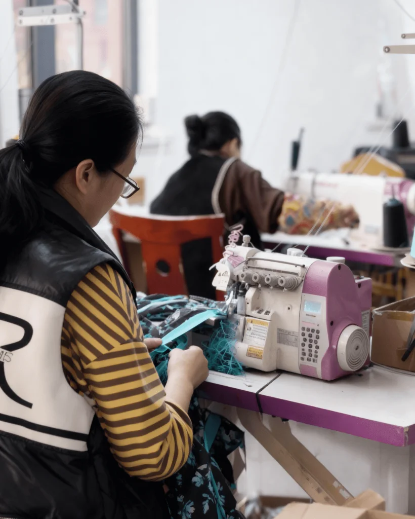 Worker operating a purple serger sewing teal and black floral swimwear fabric in a swimwear manufacturer’s production line.